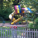 A playground with a slide and swing set in the middle of a yard.